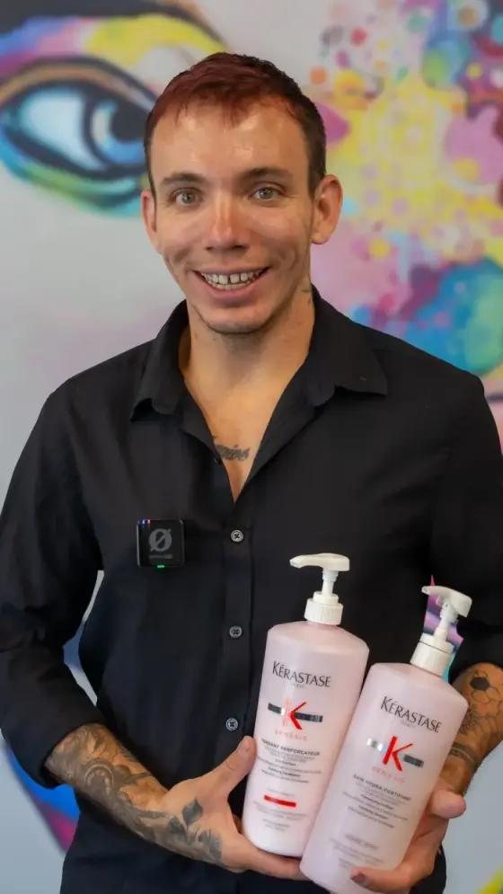 A stylist smiling and holding two bottles of salon product at his station