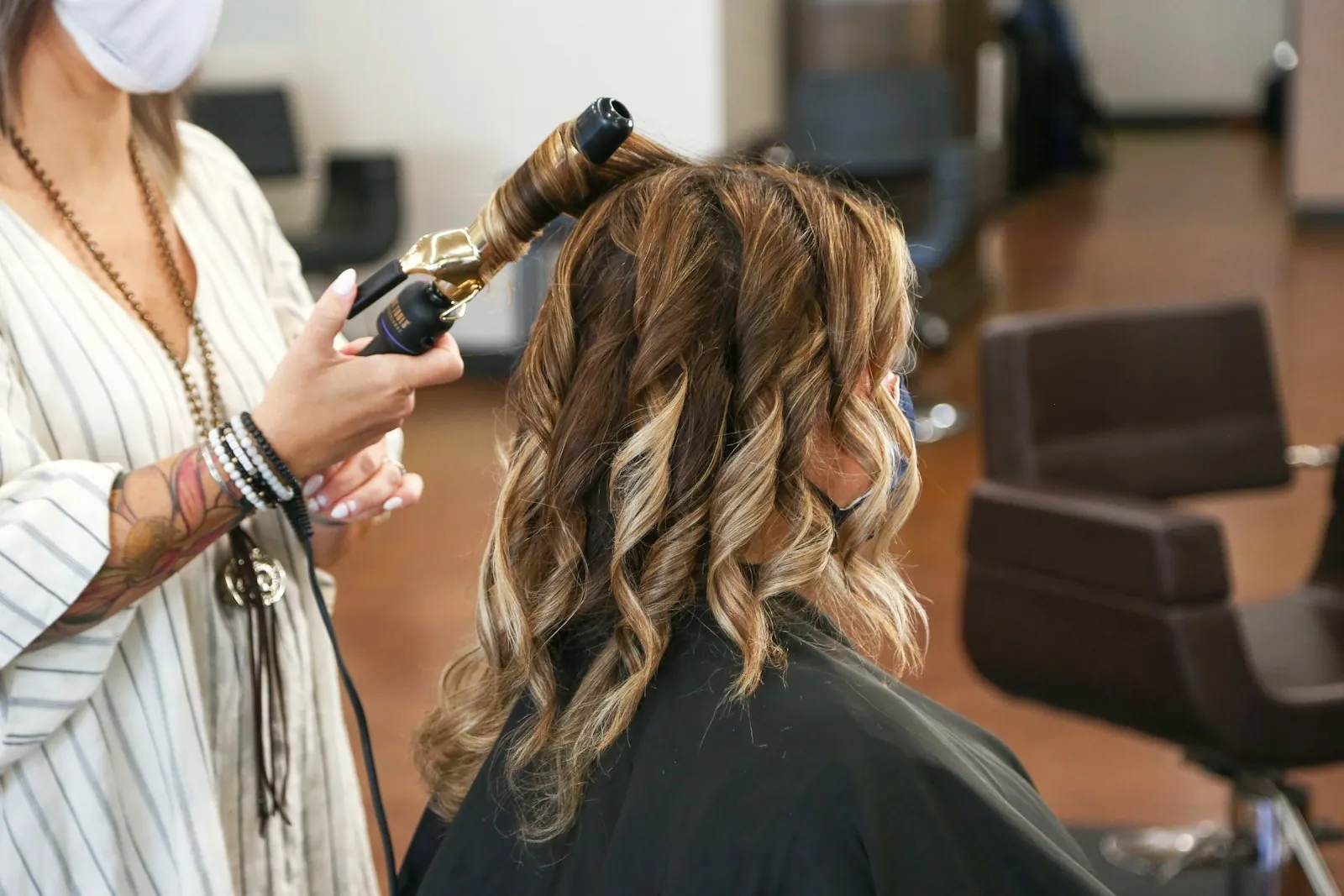 A stylist curling a client's hair with a wand at her station